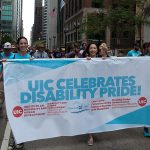 UIC DHD students, faculty and staff holding a banner in a parade that says UIC celebrates disability pride! Listed under these words: Institute on Disability and Human Development; Disability and Human Development College of Applied Health Sciences; Great Lakes ADA Center; Chancellor’s Committee on the Status of Persons with Disabilities; Disability Studies Student Council, Department of Disability and Human Development. On each side of the banner is a circle with UIC in the middle.